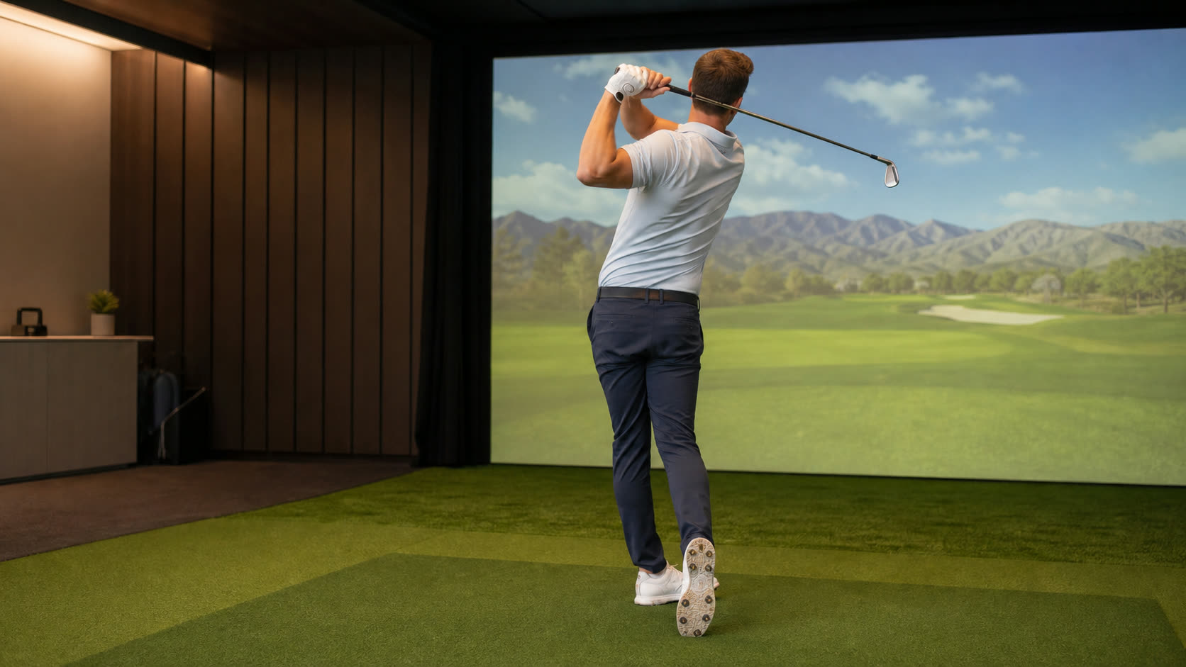 A golfer finishing tall and balanced after a full swing in an indoor simulator bay